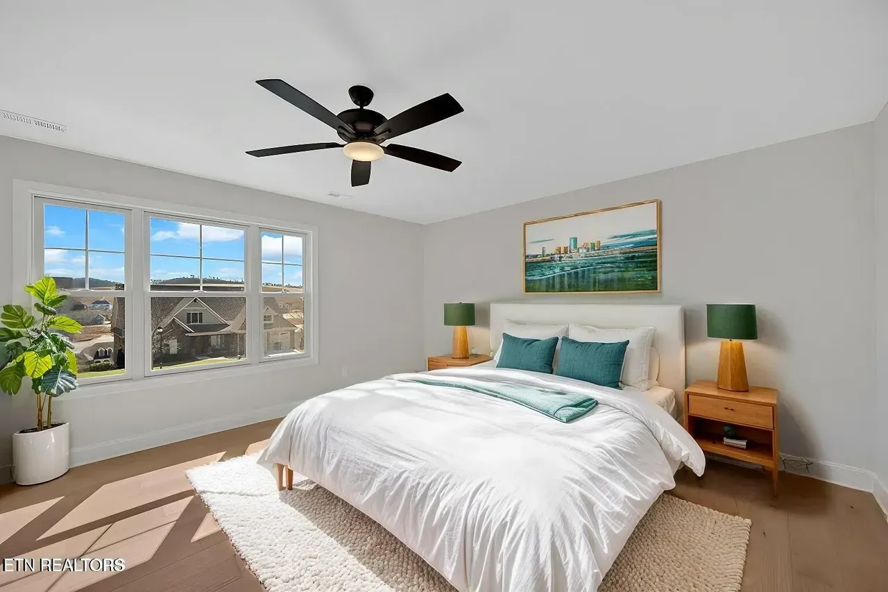 Bedroom with a bed, nightstands, window, and a ceiling fan. Bright, neutral tones.