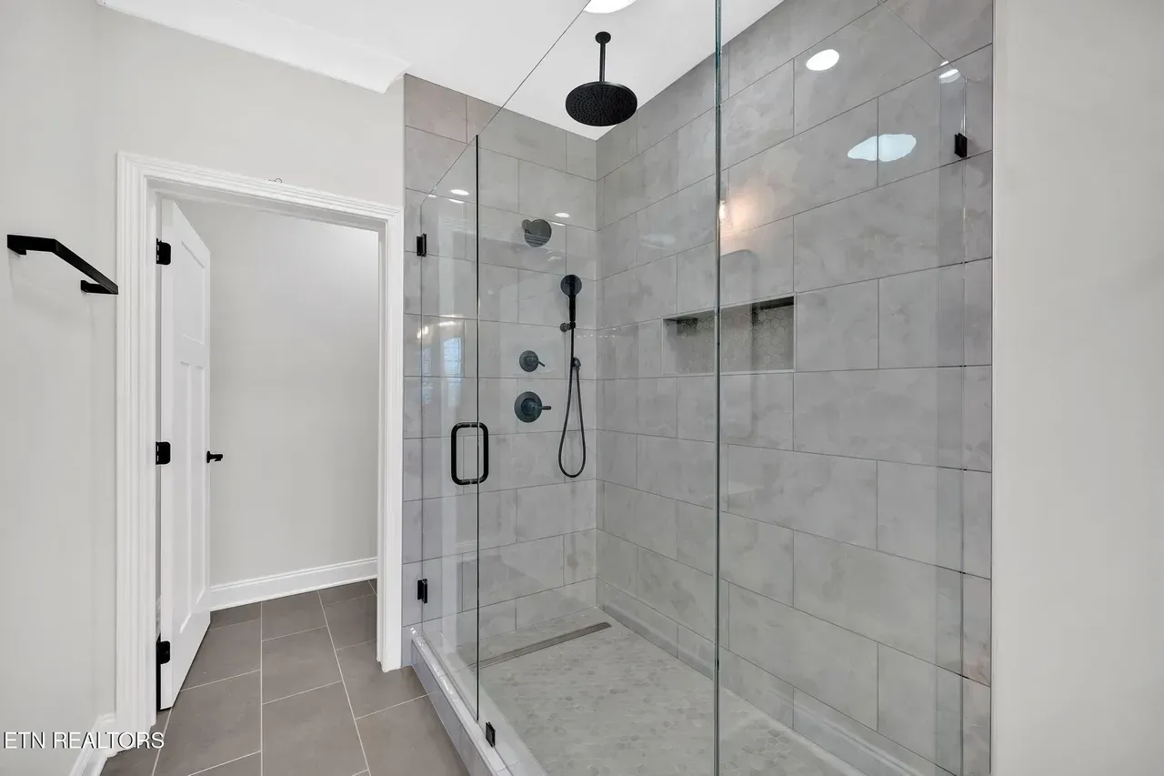 Modern bathroom with glass shower, gray tiled walls, black fixtures, and a recessed niche.