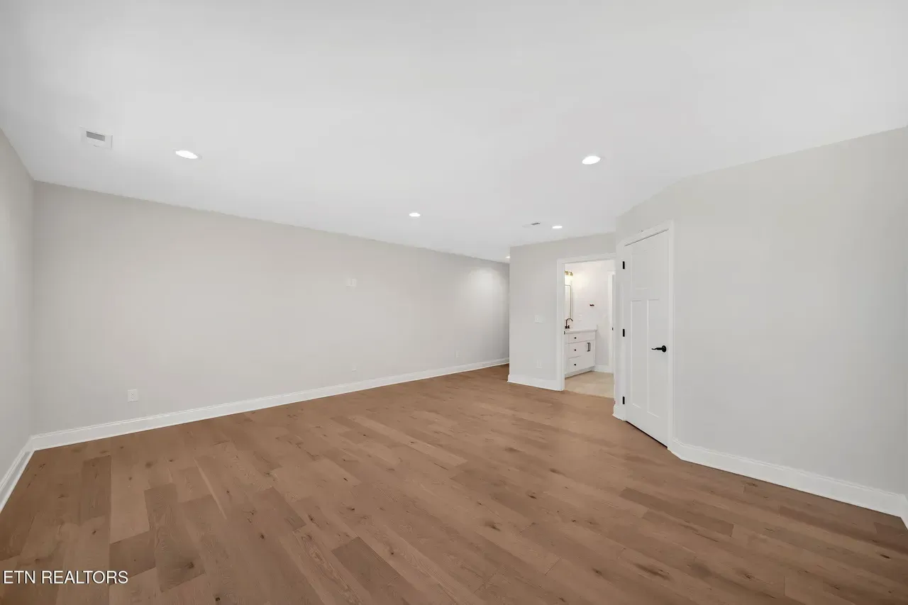 Empty room with hardwood floors, white walls, and a doorway leading to a bathroom.