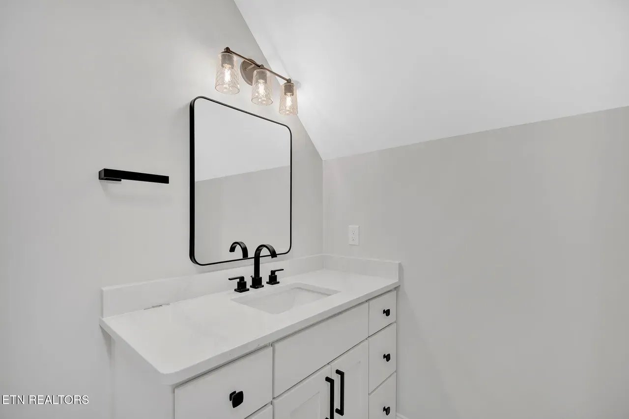 Bathroom with white vanity, black faucet, mirror, light fixture, and gray walls.