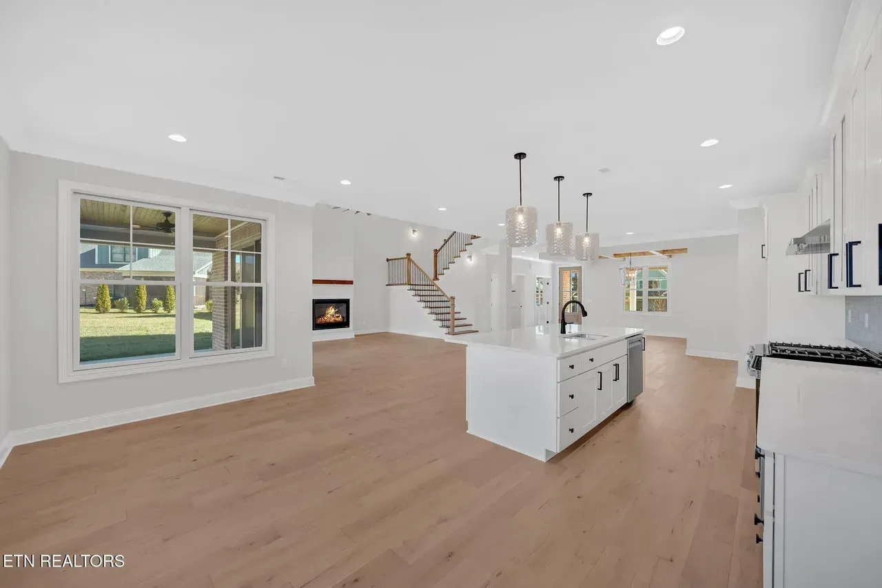 Open-concept living space with a kitchen island, fireplace, and stairs. Large windows offer an outdoor view.