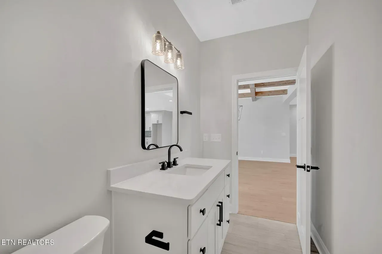 Bathroom with white vanity, black faucet and mirror frame, toilet, and open doorway to a closet.