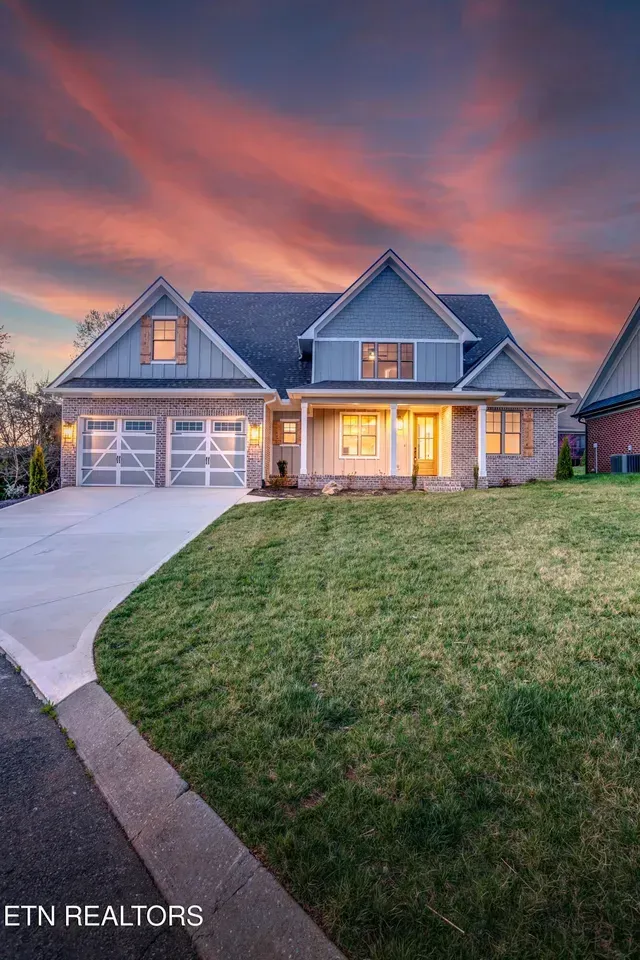 House exterior with blue and brick facade, two-car garage, and green lawn under a sunset sky.