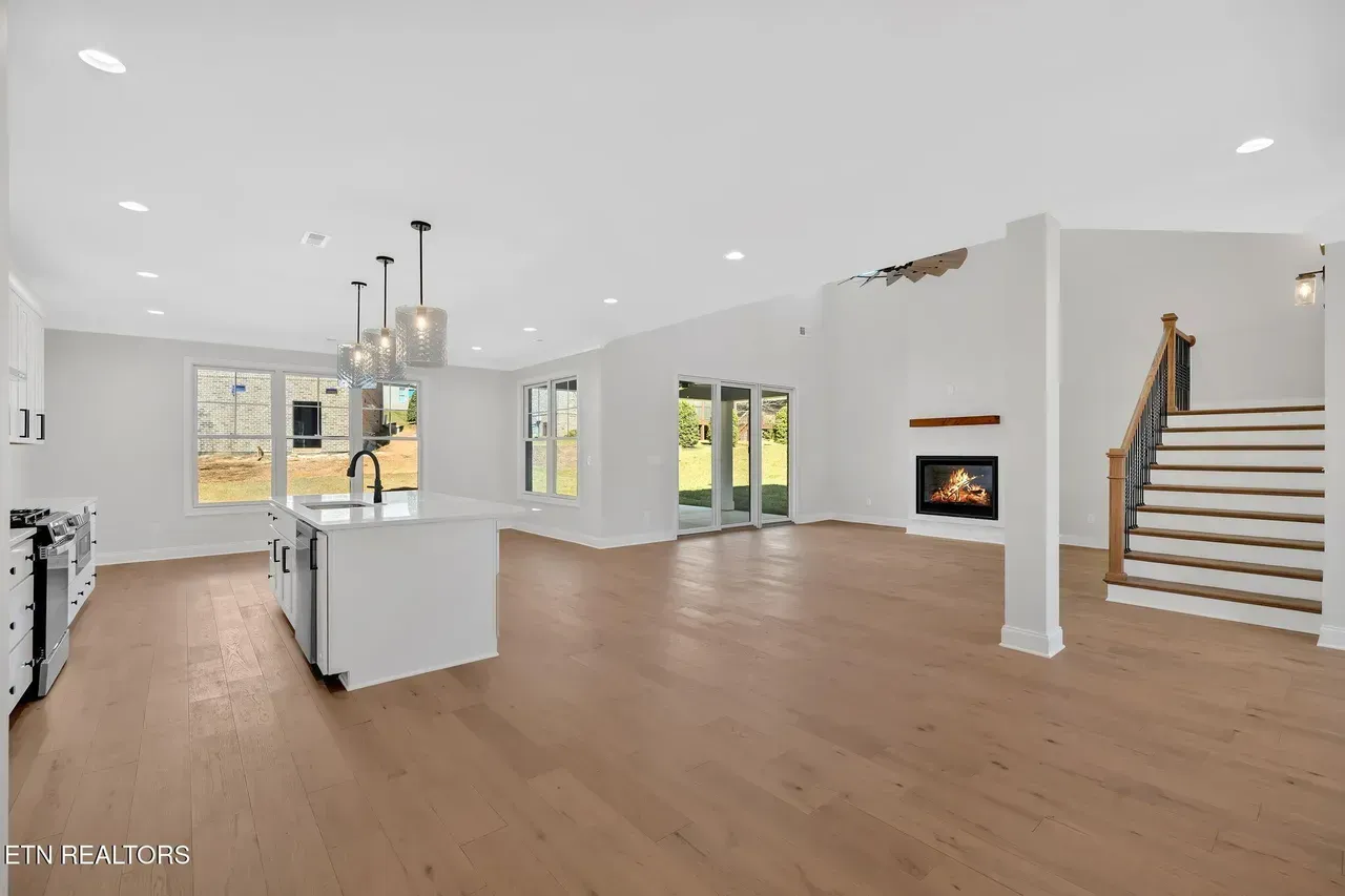 Open-concept living space with kitchen island, fireplace, and staircase; wood floors, white walls.
