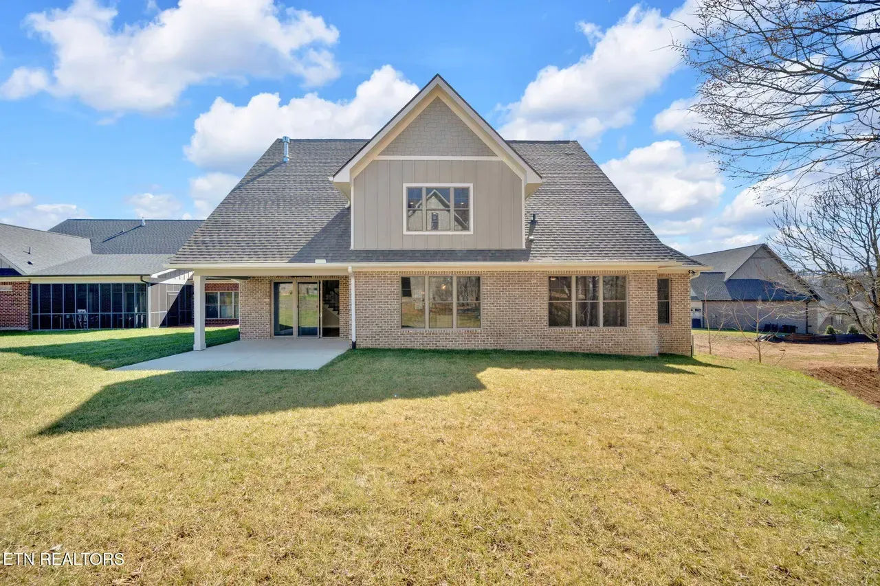 Back of a beige brick house with a grassy yard, under a blue sky with clouds.