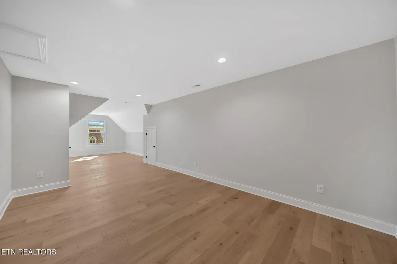 Empty room with light-colored hardwood floors and gray walls. Includes a small window and a doorway.