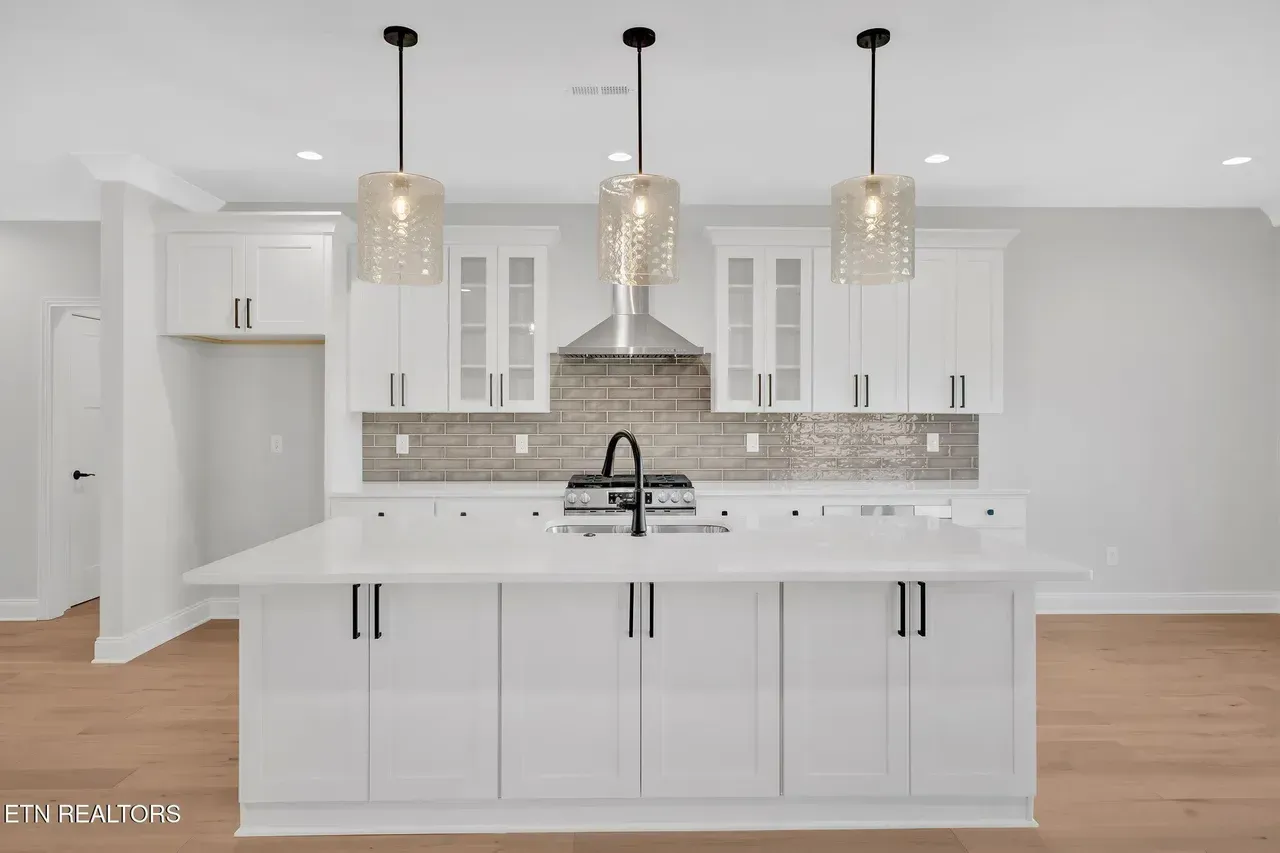 White kitchen with island, pendant lights, and stainless steel backsplash.