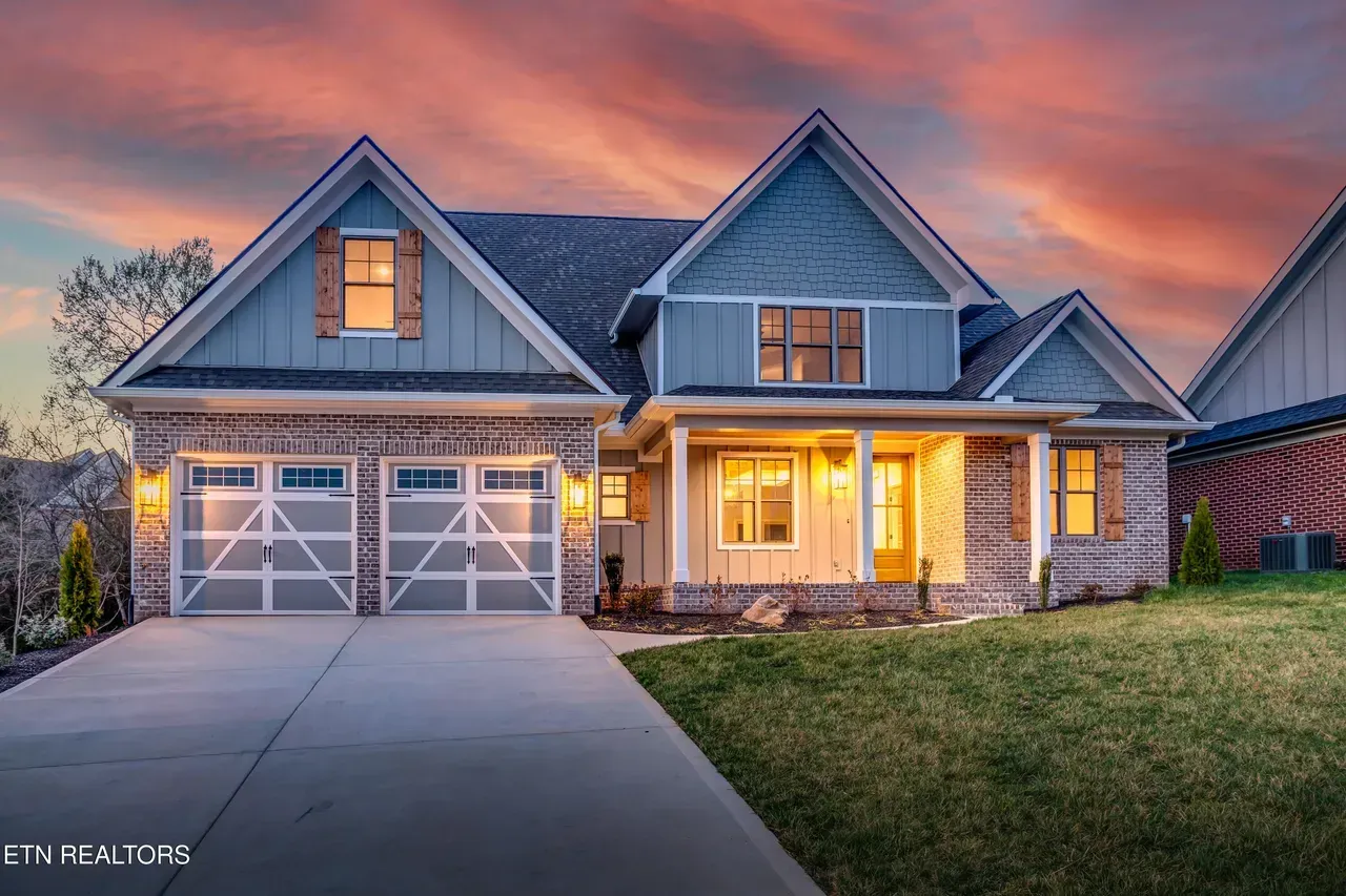Blue and brick home with two-car garage, porch, and dusk sky.