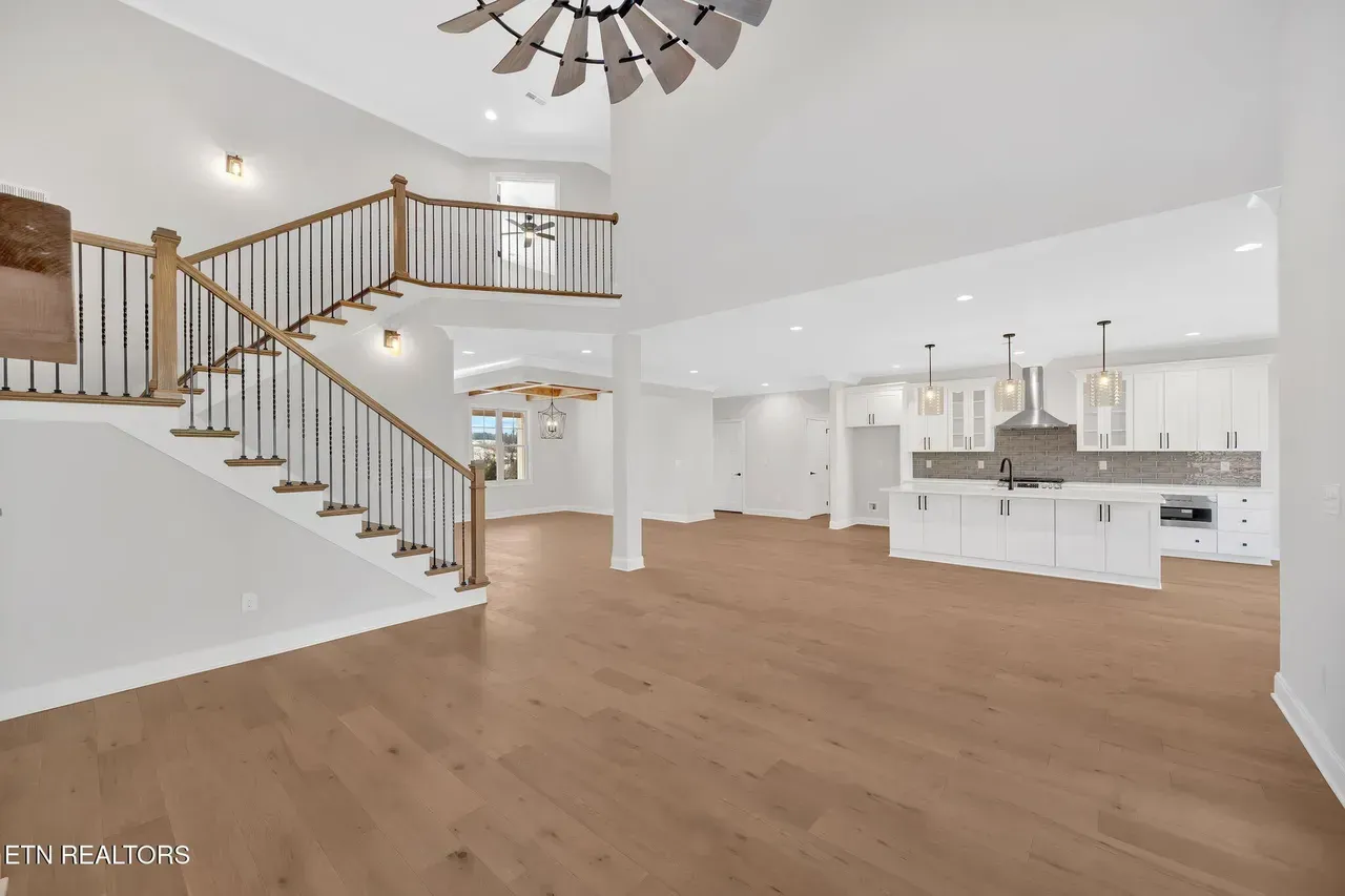 Spacious, bright interior with hardwood floors, staircase with black railing, and white kitchen with island.