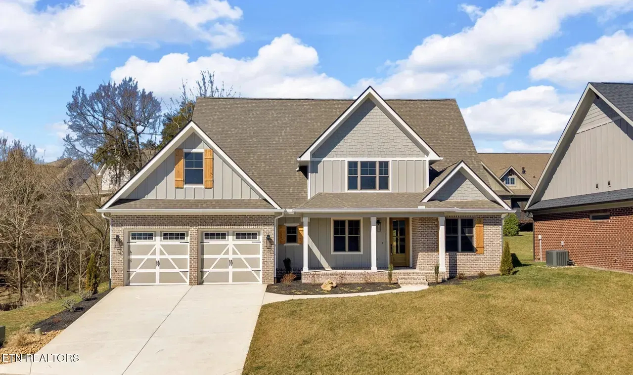 Two-story house with gray siding, brick accents, and a driveway on a sunny day.