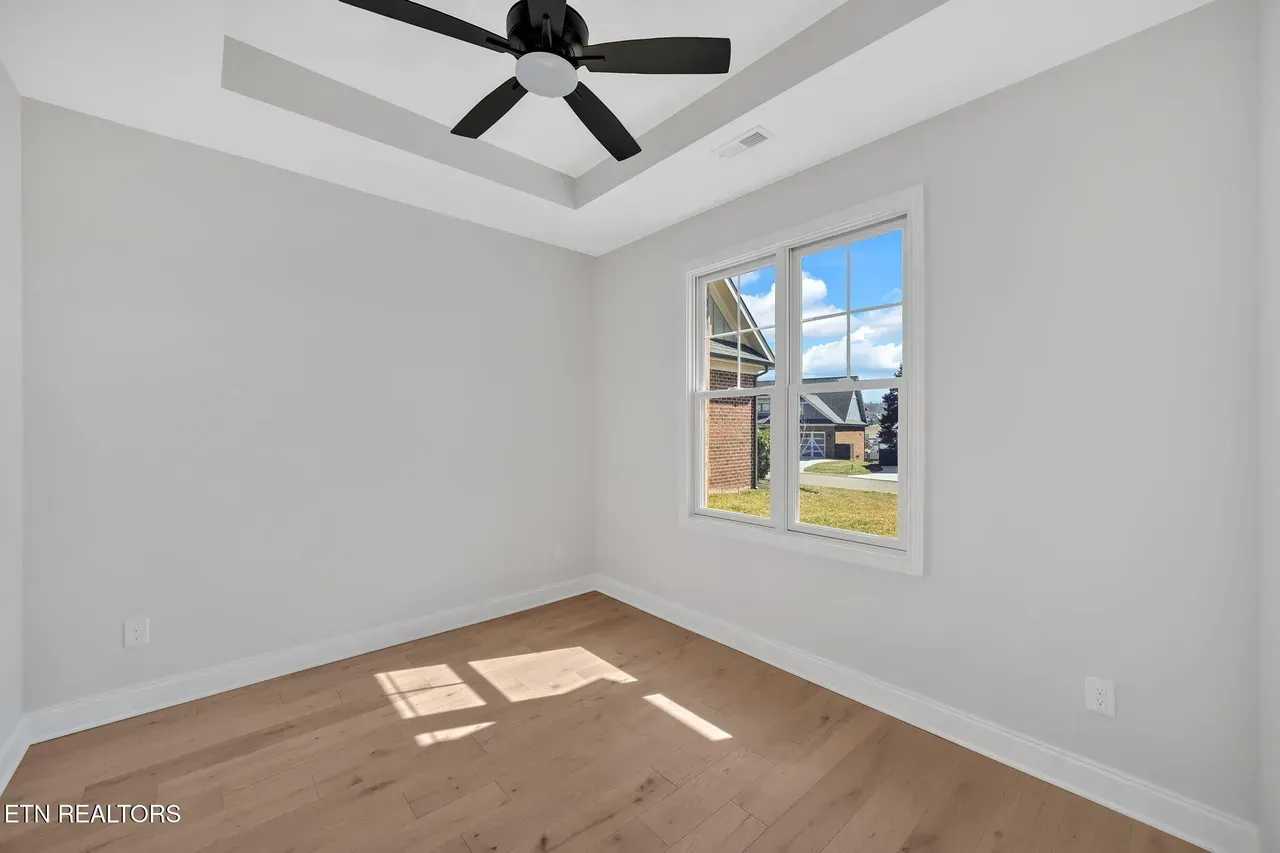 Empty room with wooden floors, white walls, ceiling fan, and window with a view.