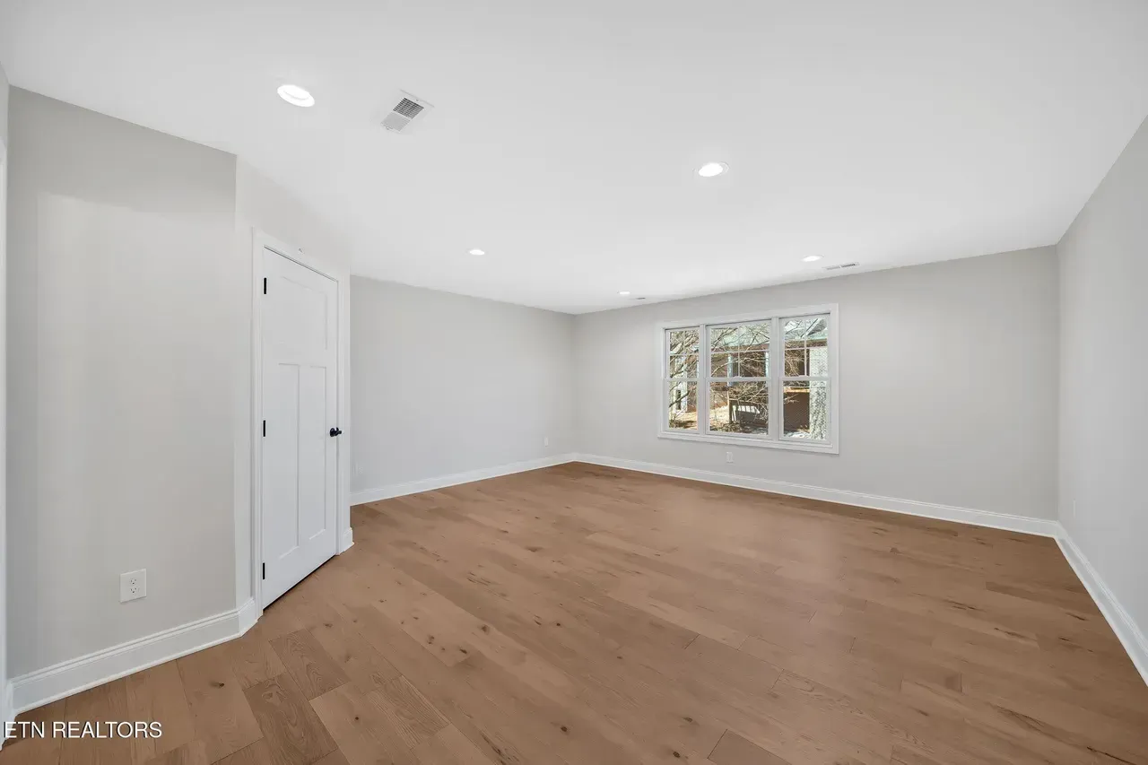 Empty room with hardwood floors, light gray walls, white trim, and a window.