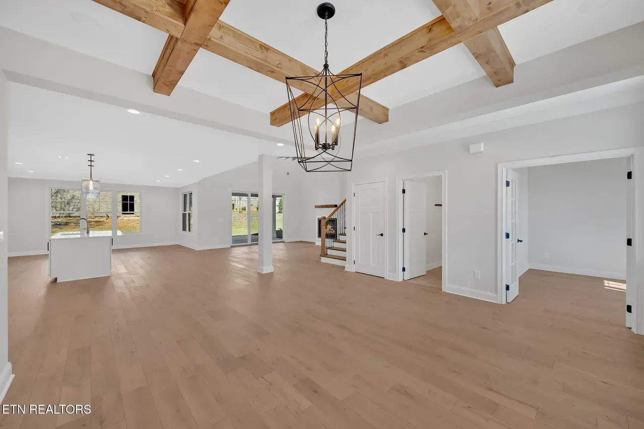 Spacious, light-filled interior with exposed wooden beams, hardwood floors, and a modern chandelier.