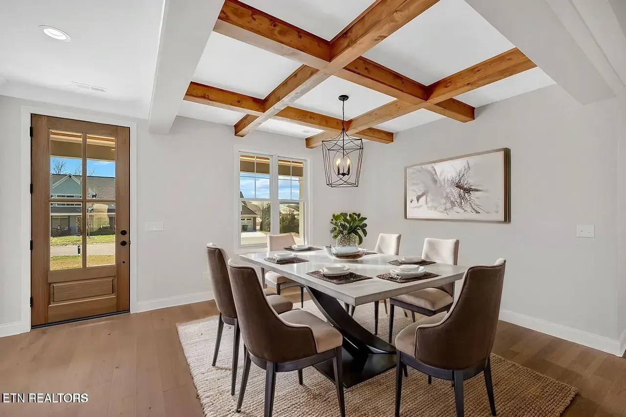 Dining room with wooden beams, table set for six, and a view through the window.