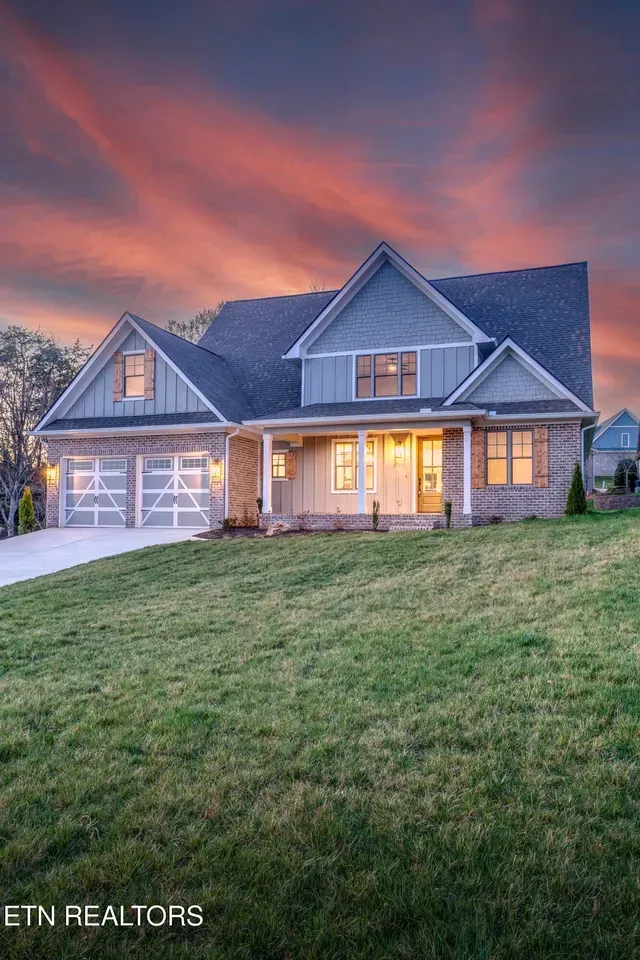 Two-story house with gray and brick facade at dusk with a colorful sky. Green lawn in the foreground.