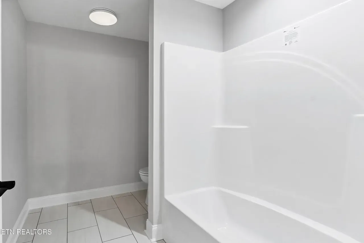 Bathroom with a white tub and shower surround, light gray walls, and white and gray floor tiles.