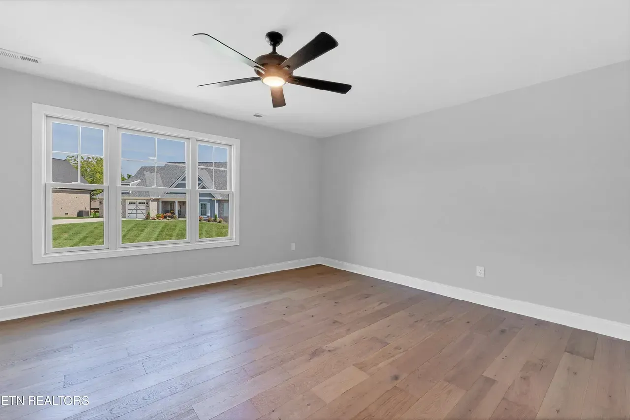 Empty room with hardwood floors, gray walls, large window with a view, and ceiling fan.