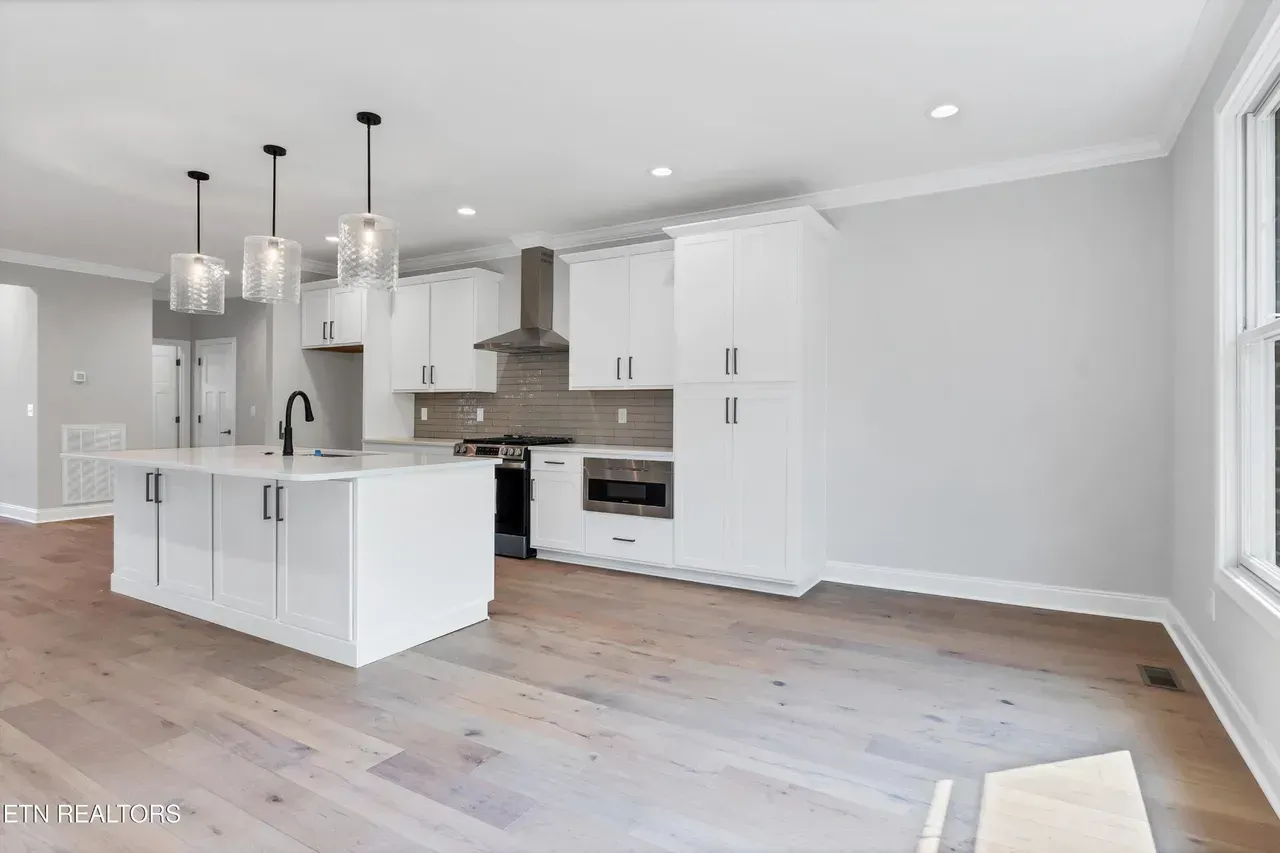 Modern white kitchen with island, stainless steel appliances, and wood floors.