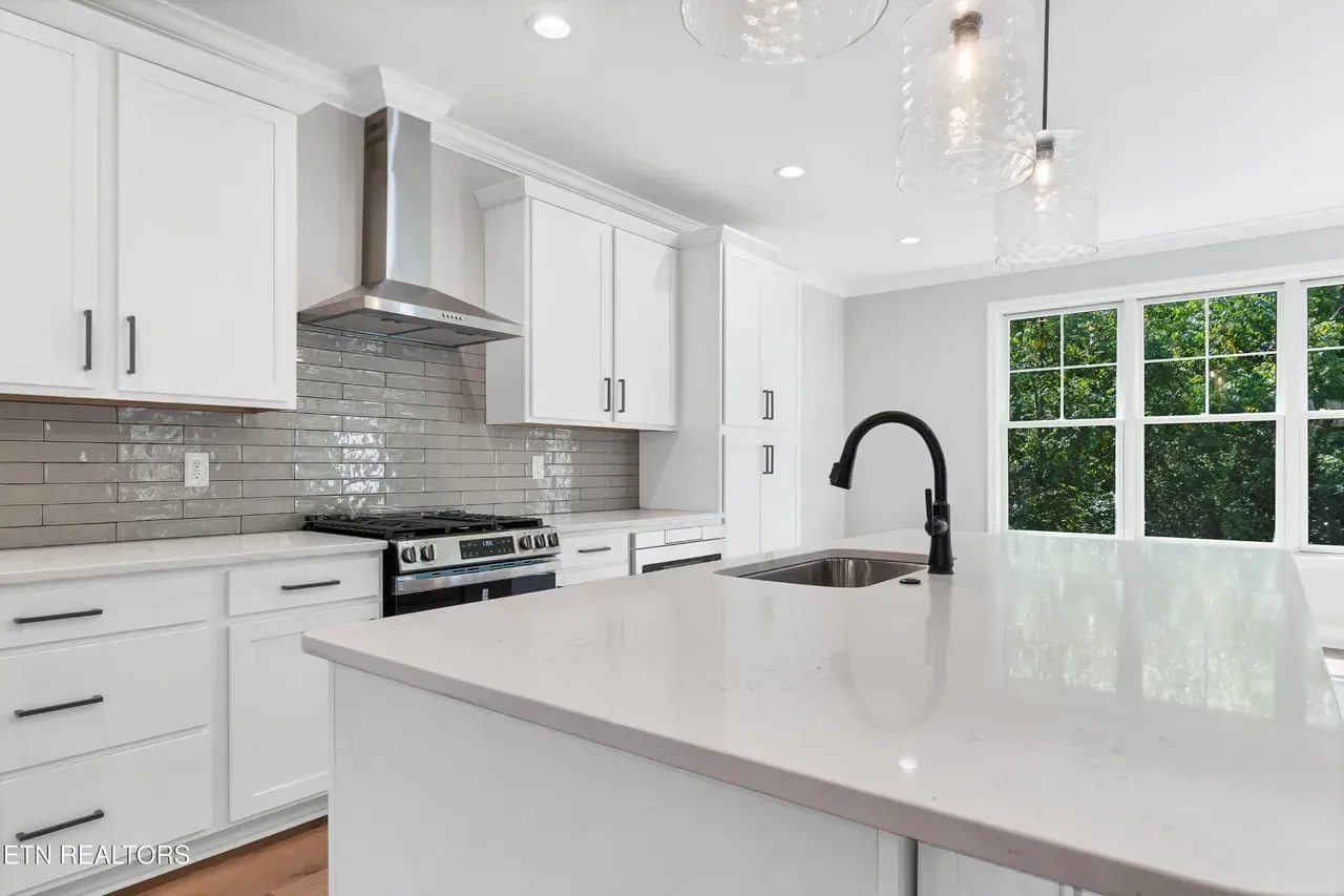 Modern white kitchen with stainless steel appliances, large island, and bright window.