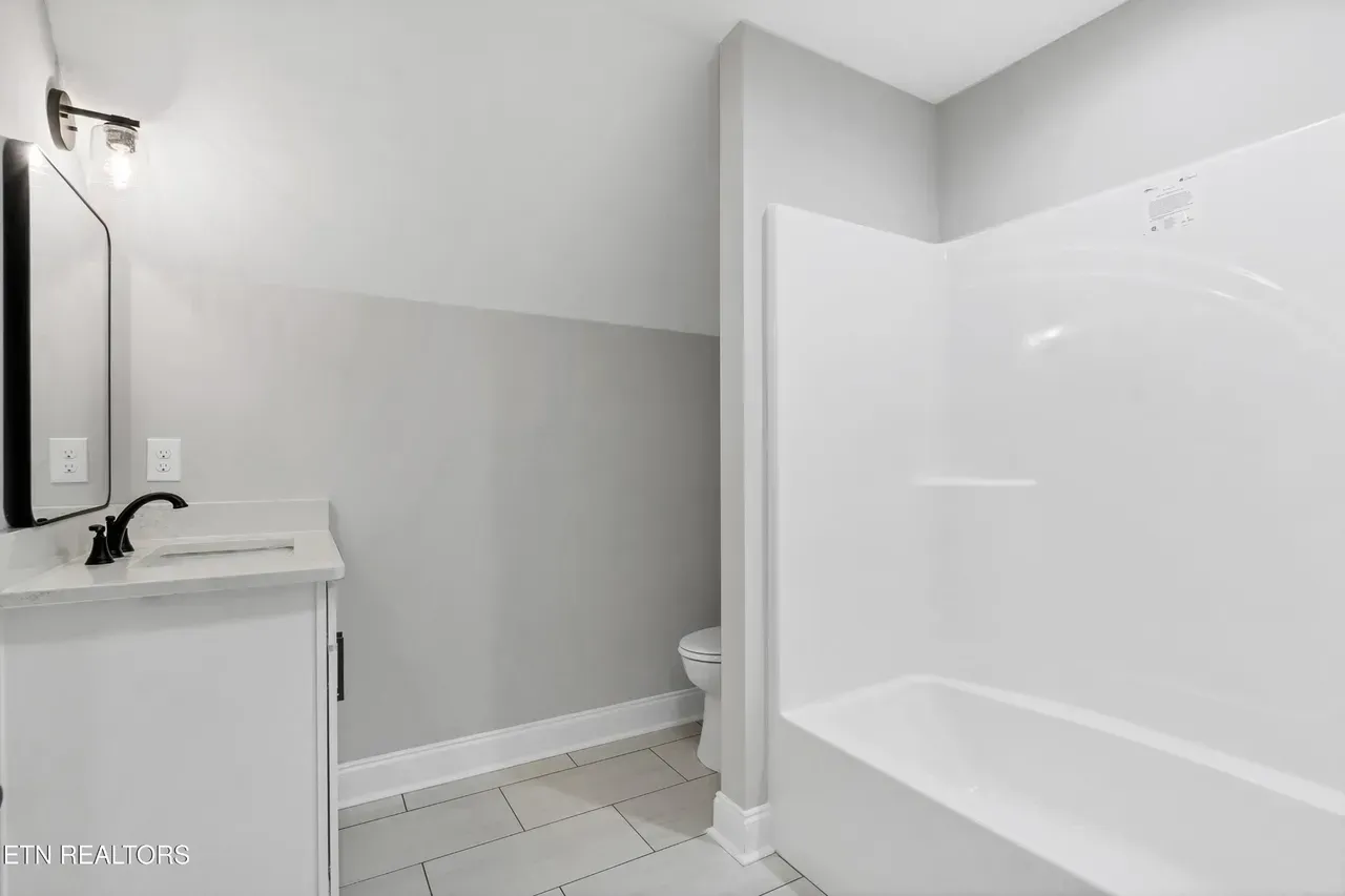 Bathroom with white tub, vanity, and toilet; gray walls and floor.