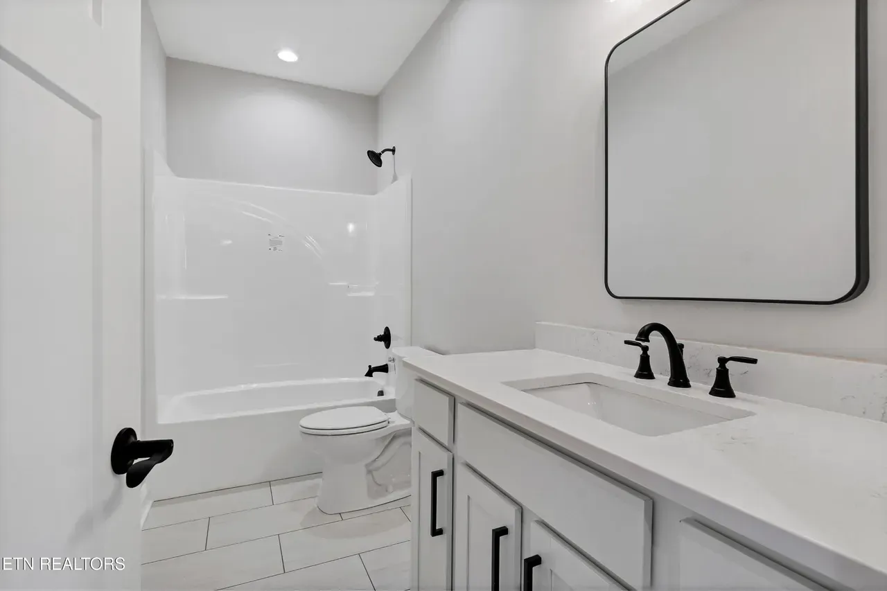 Modern white bathroom with vanity, mirror, shower/tub, and black hardware.