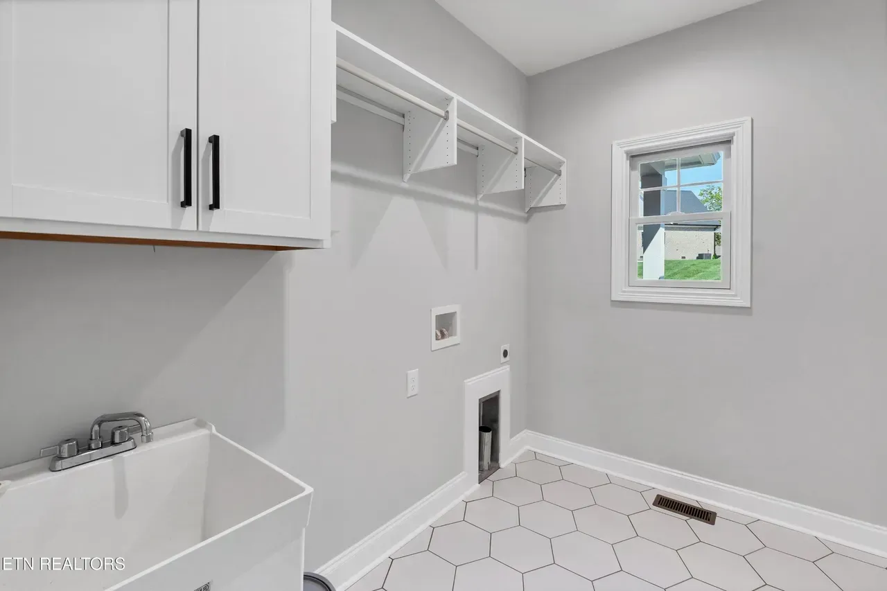 Laundry room with white cabinets, utility sink, and hexagonal tile flooring. Light gray walls, window, and drying rack.