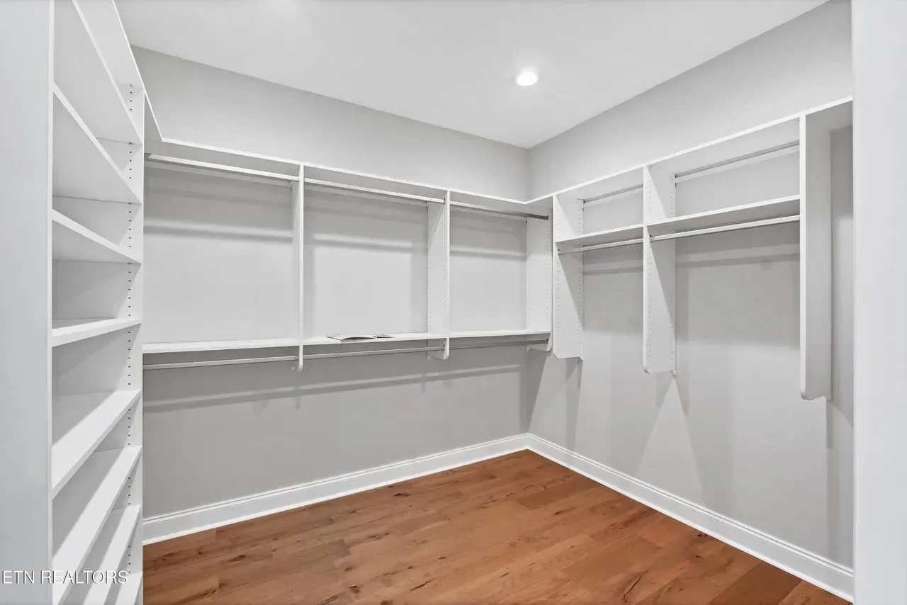 Empty white walk-in closet with wooden floors, built-in shelves, and hanging rods.