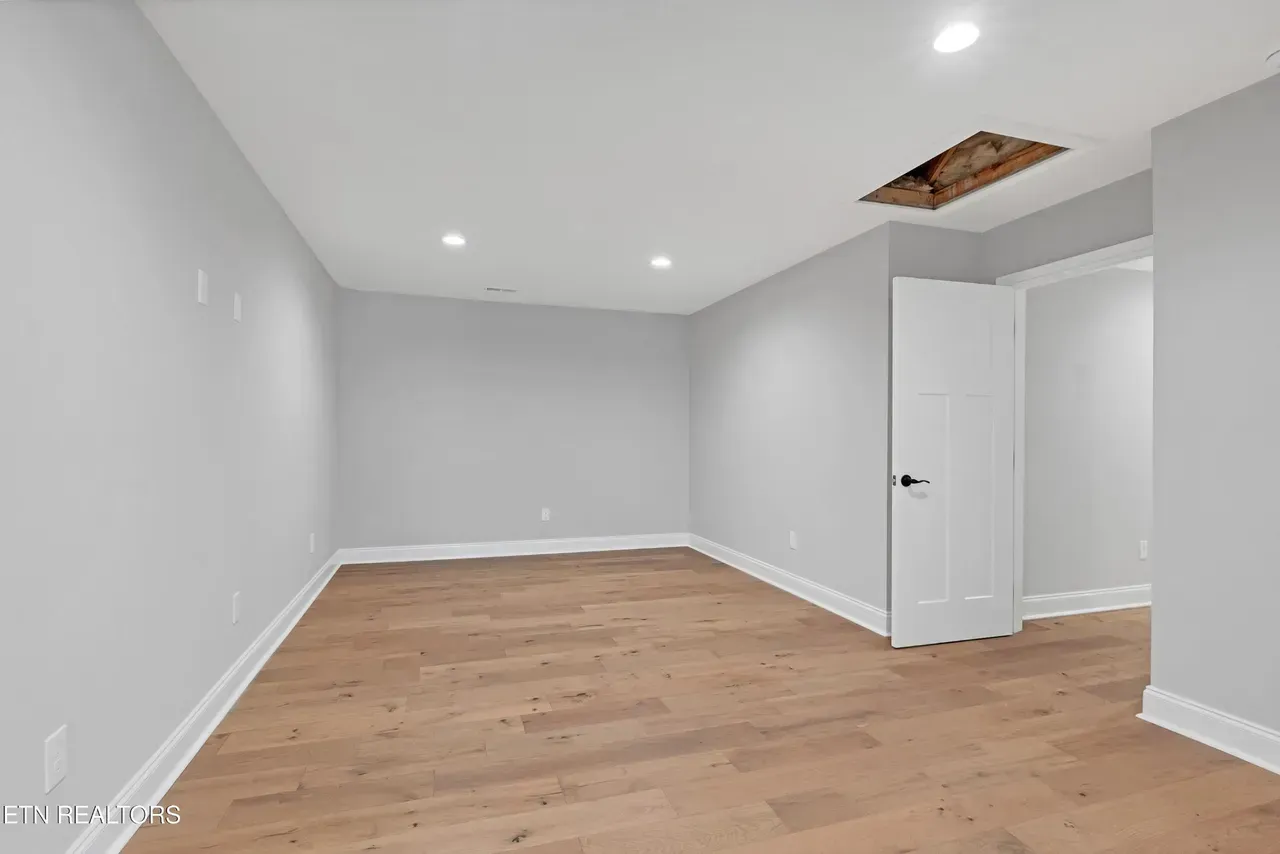 Empty room with light gray walls, wooden floor, white door, and a hole in the ceiling.
