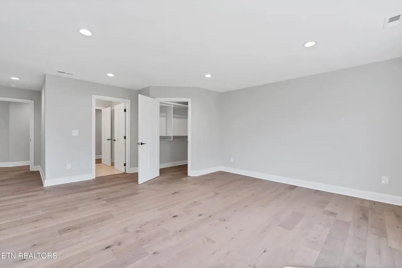 Empty room with light wood floors, gray walls, recessed lighting, and white doors.