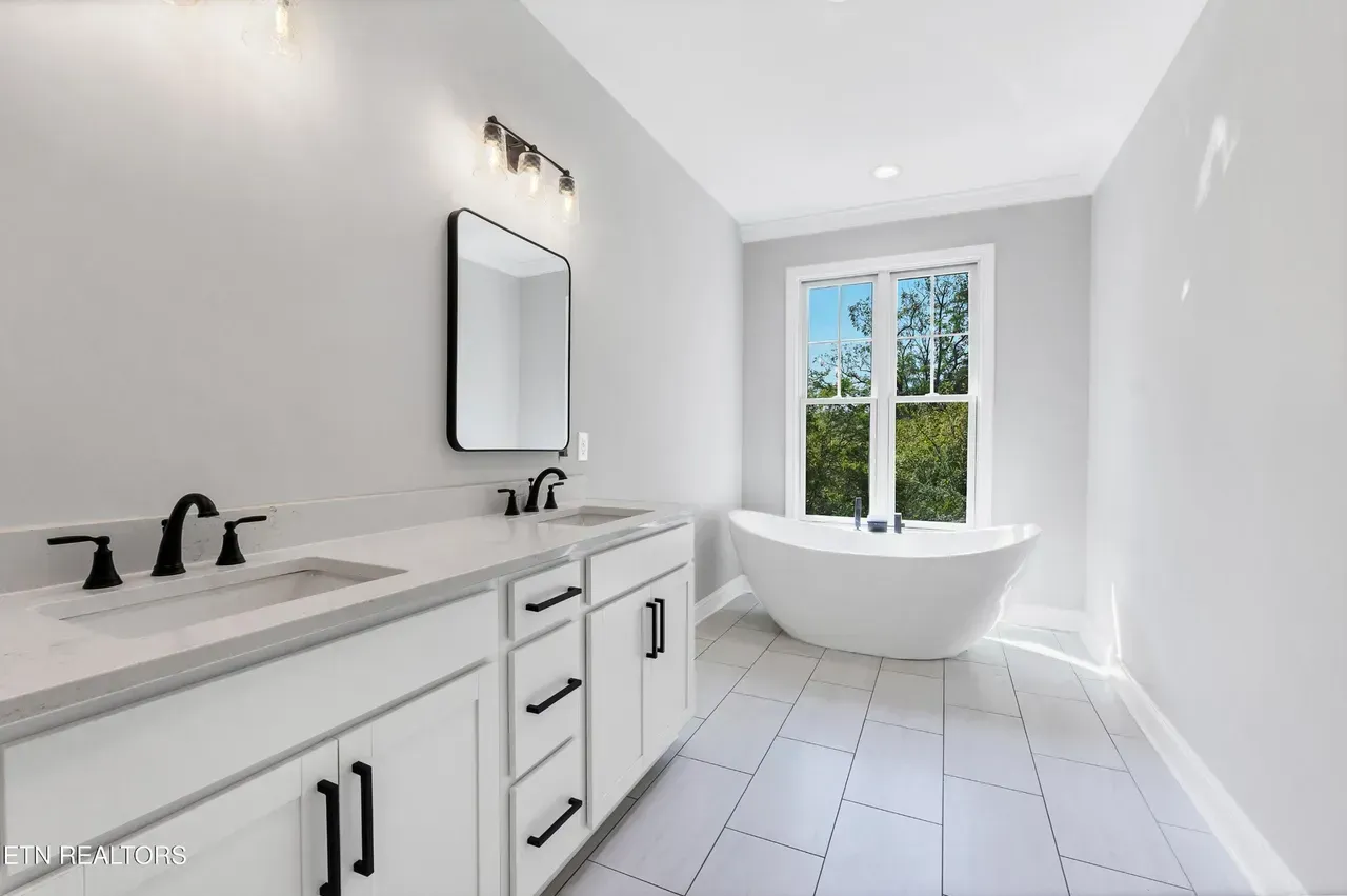 Modern bathroom with white cabinets, black fixtures, and a freestanding tub near a window.