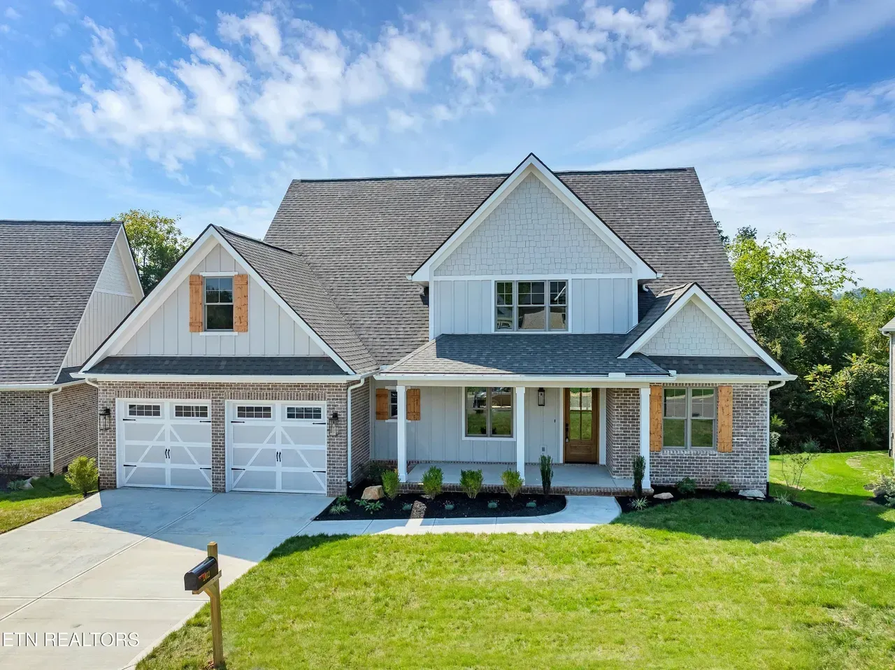 Two-story house with light blue siding, gray roof, white garage doors, and a small front yard.