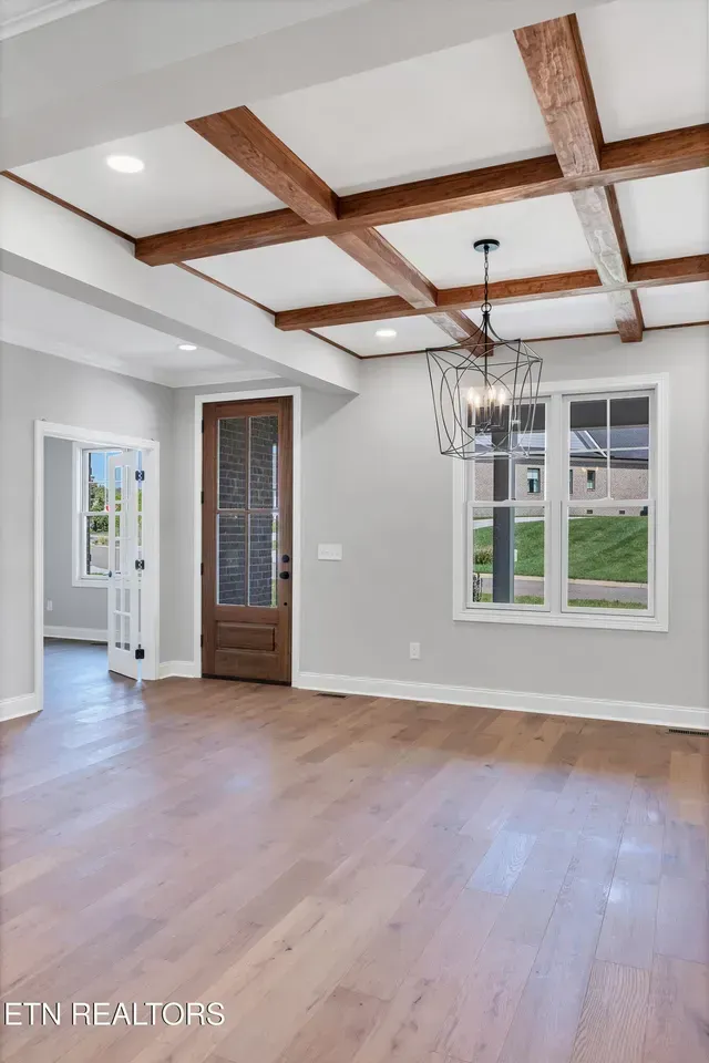 Dining room with wooden beams on the ceiling, hardwood floors, and a decorative chandelier.