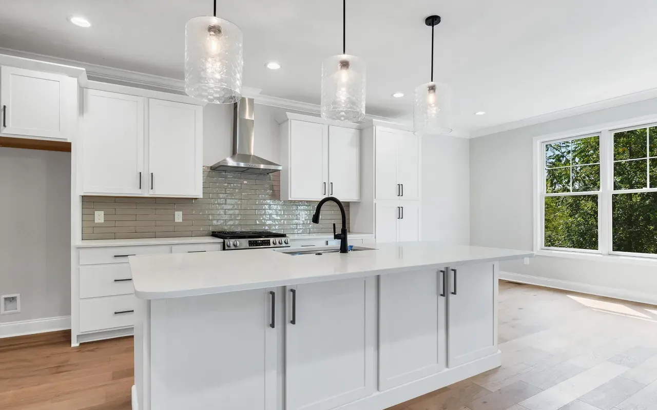 White kitchen with island, pendant lights, stainless steel appliances, and large window.