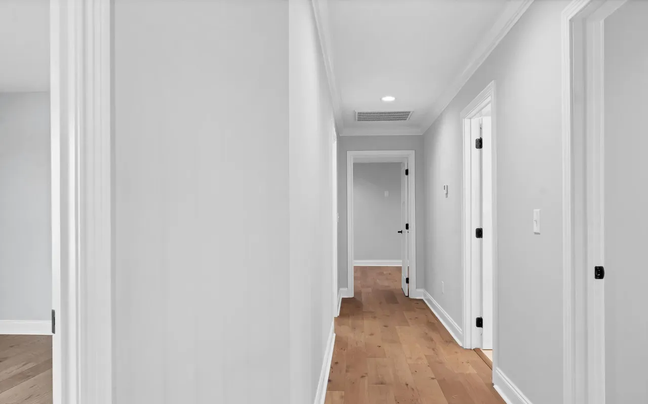 Narrow hallway with light gray walls, white trim, and wood flooring. Several doorways lead off the hall.