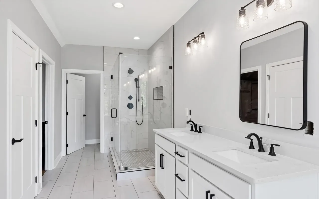 Bright, modern bathroom with white cabinetry, glass shower, and black fixtures.