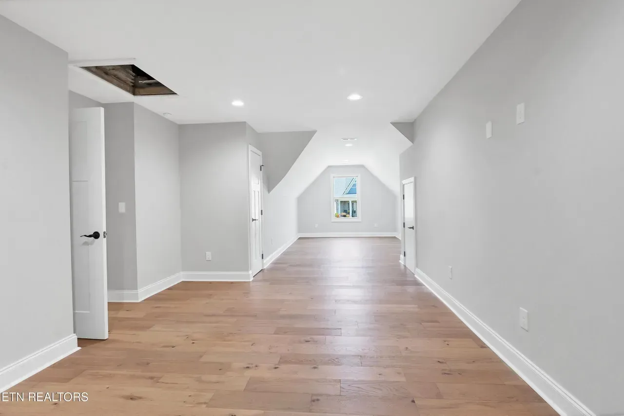 Empty room with hardwood floors, light gray walls, and a small window at the end.