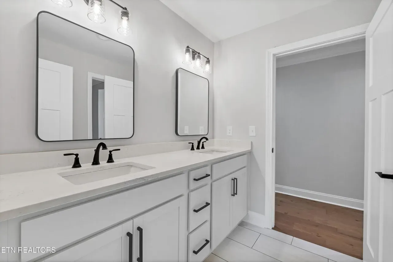 Modern bathroom with white cabinets, countertops, and gray walls; black fixtures, mirrors, and lighting.
