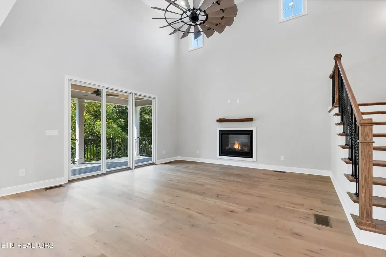 Spacious living room with high ceilings, fireplace, and sliding glass doors leading to a wooded view.