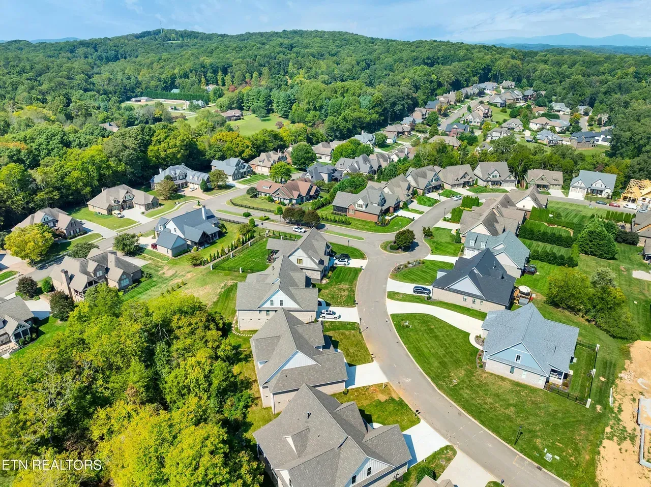 Aerial view of a suburban neighborhood with houses, roads, and lush green trees on a hillside.