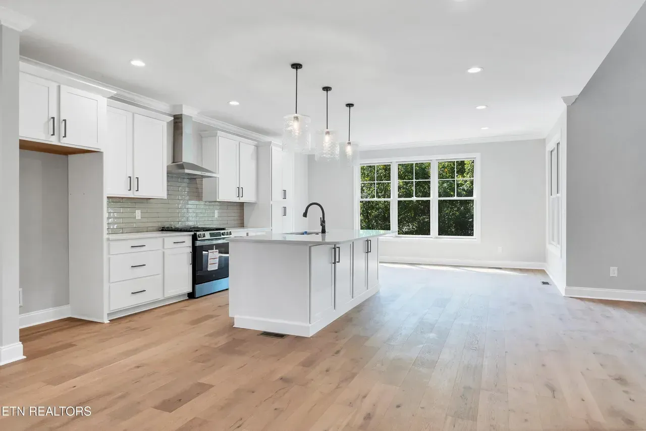 Modern white kitchen with island, wood floor, and large window.