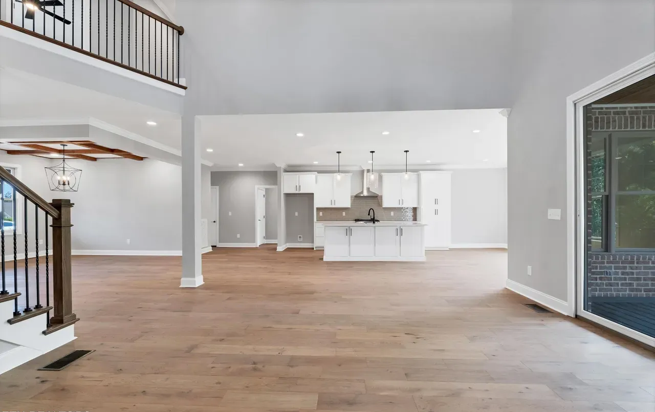 Open-concept home interior with hardwood floors, white kitchen, and a staircase.
