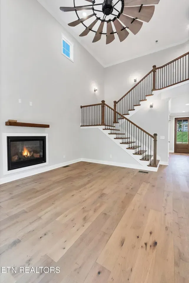 Spacious living room with fireplace, staircase, and hardwood floors. Modern, neutral tones.