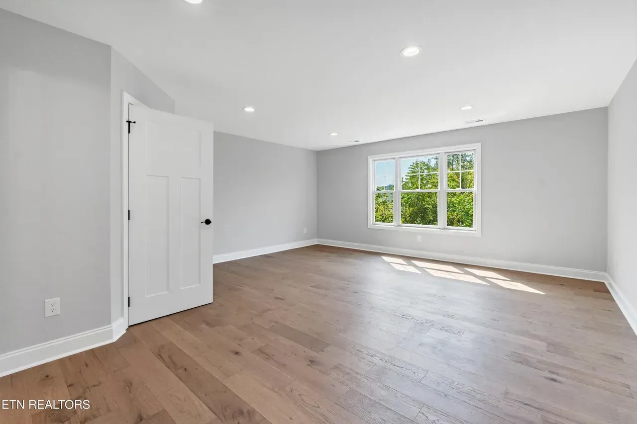 Empty room with hardwood floors, a white door, and a window with a view of greenery.