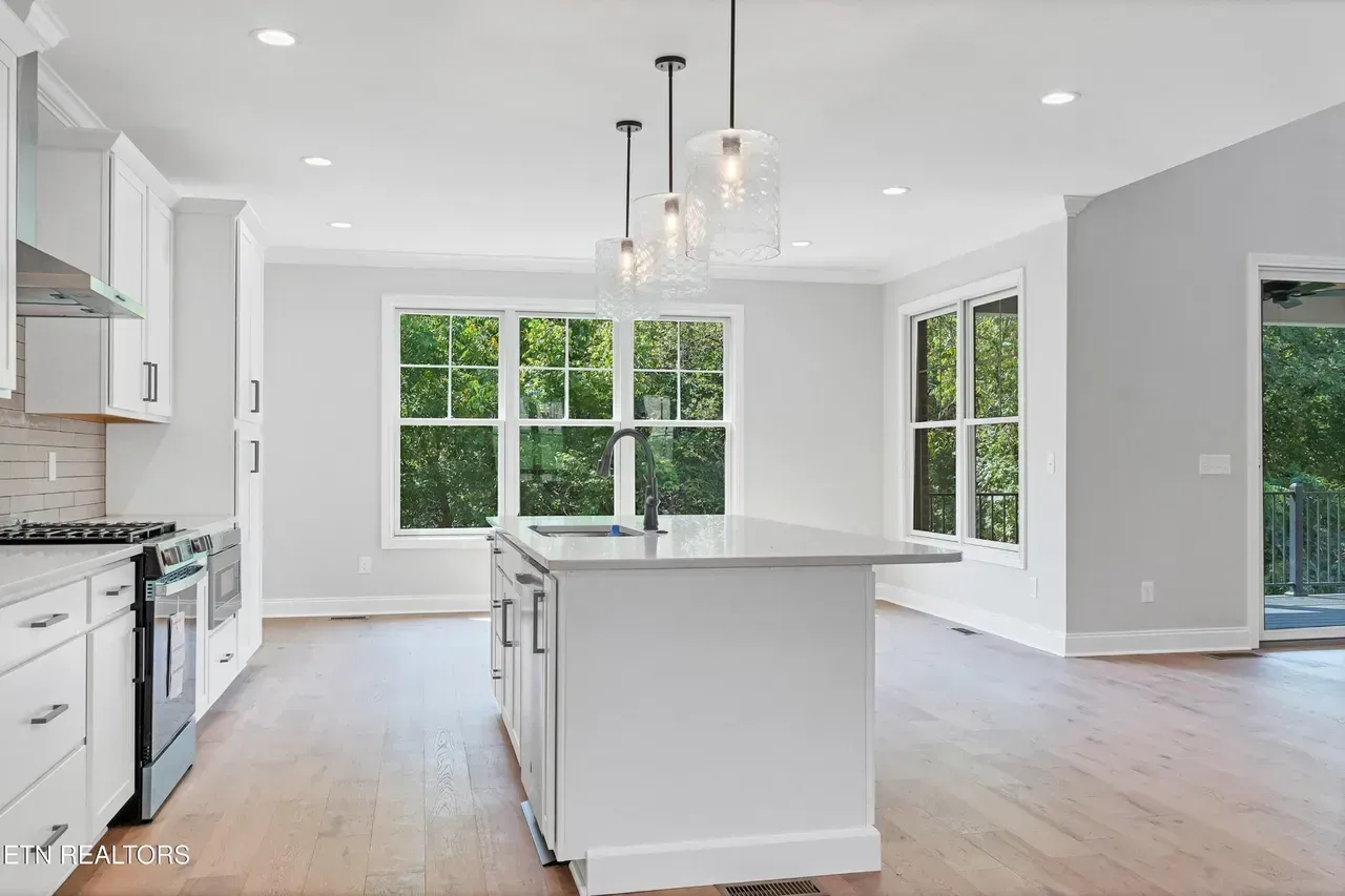 Modern white kitchen with island, hardwood floors, large windows with natural light.