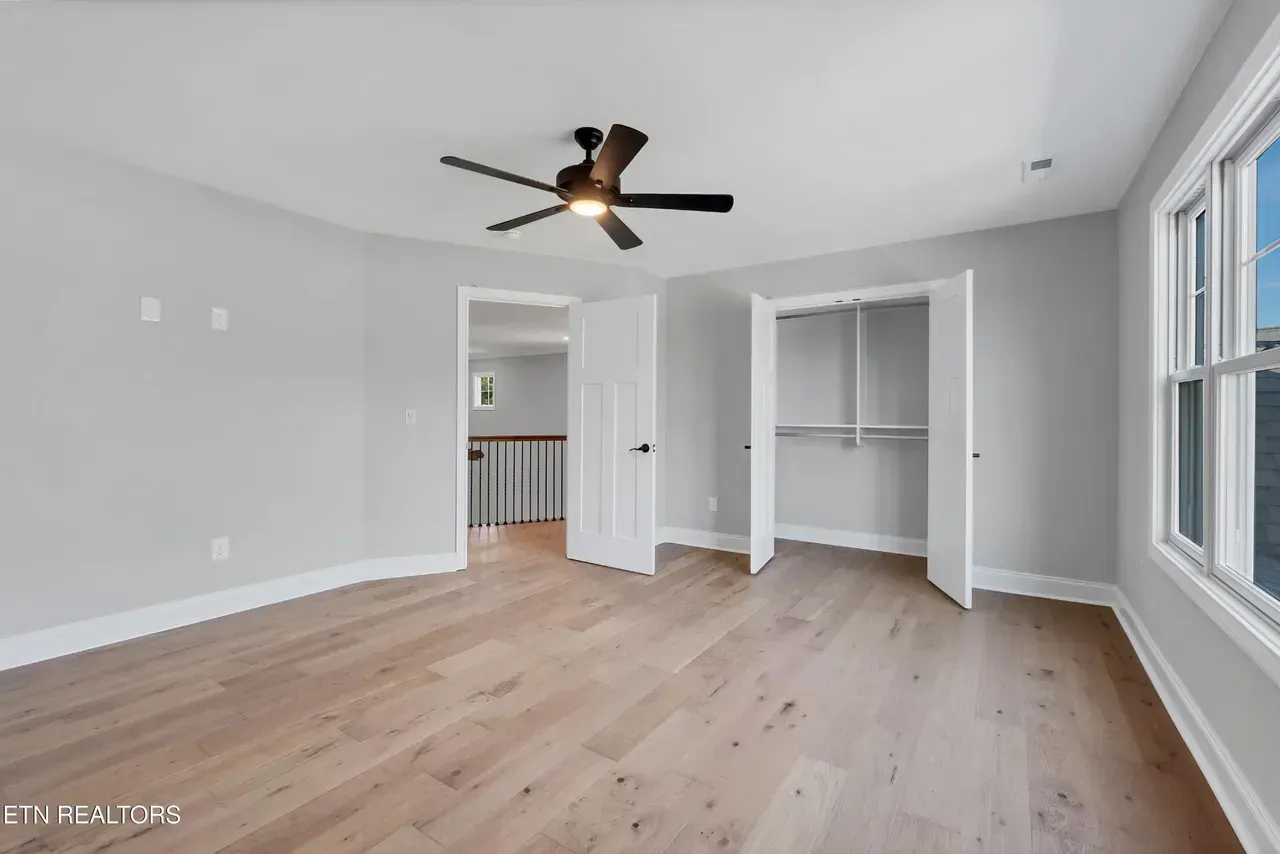 Bedroom with light wood flooring, gray walls, closet, and a ceiling fan.