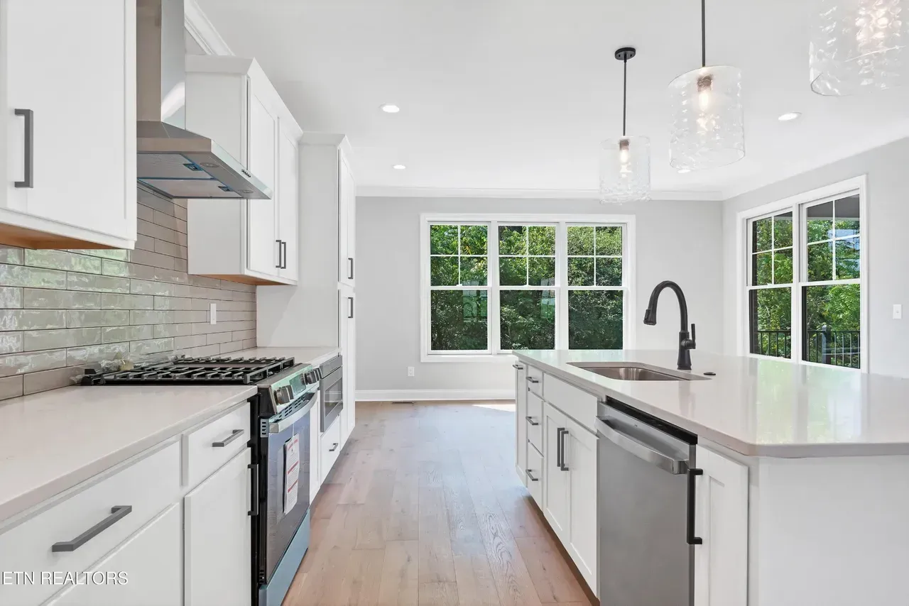 Modern white kitchen with stainless steel appliances, island, and large windows.