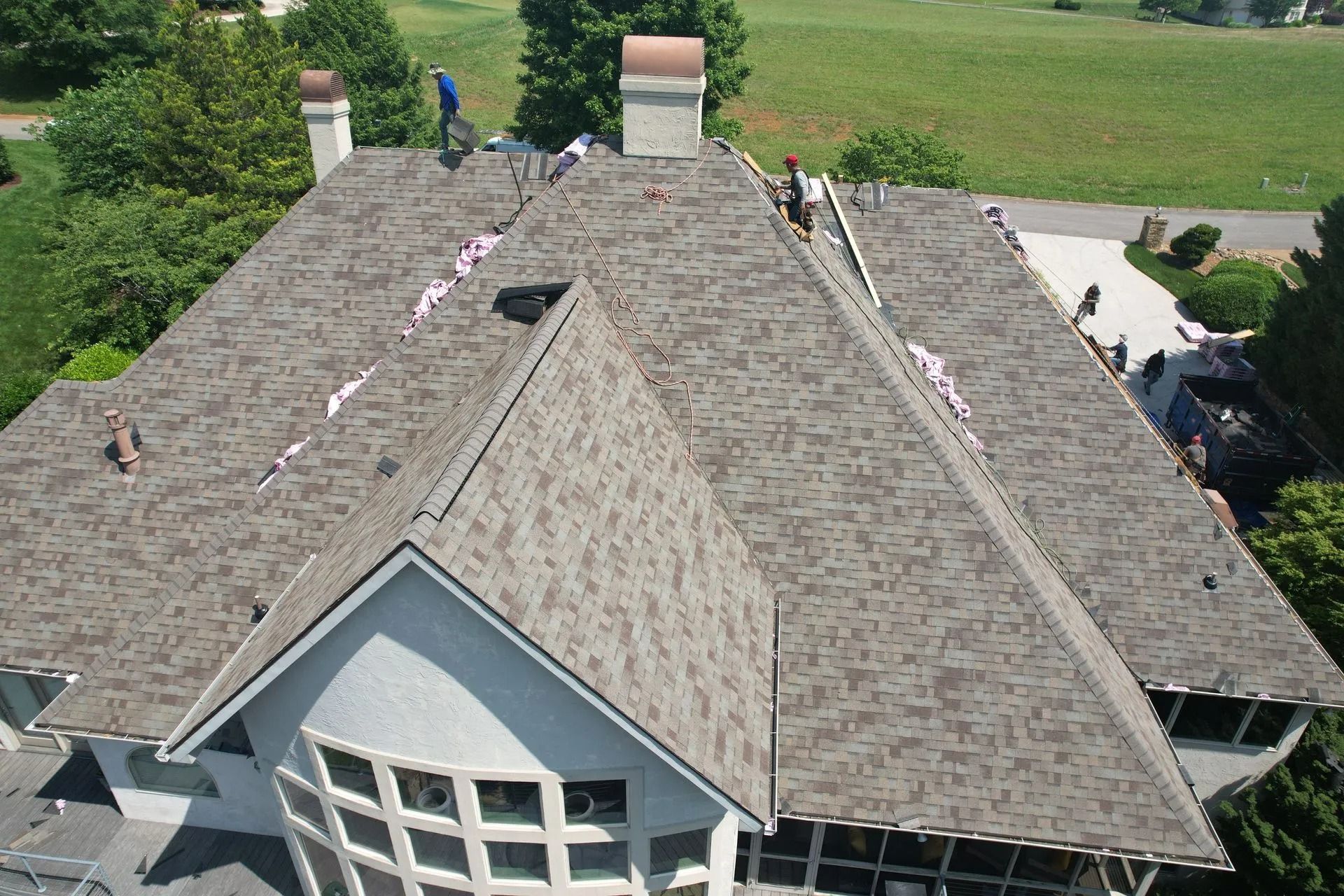 Roofers working on a residential roof, with shingles and a chimney visible.