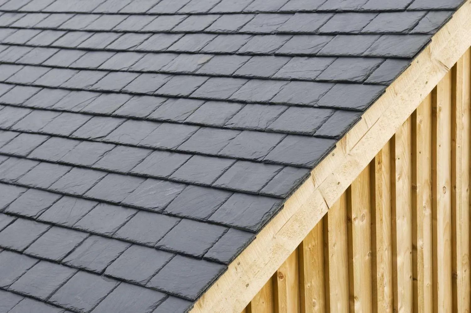 Close-up of a roof with dark gray slates next to light brown wooden siding.