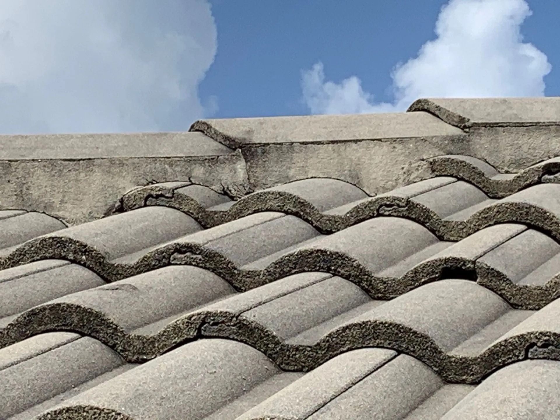 Gray concrete roof tiles against a blue sky with clouds.