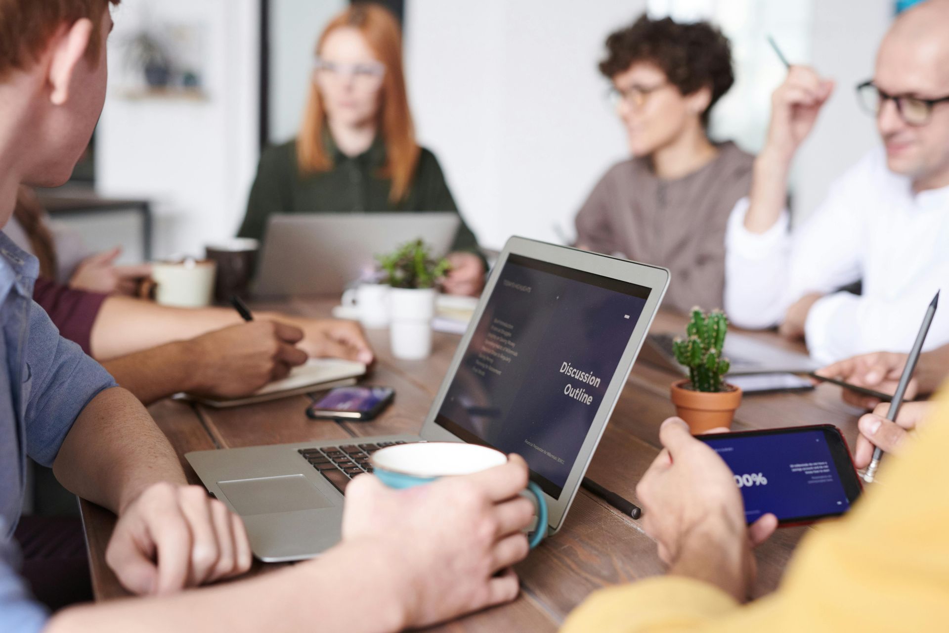 Un grupo de personas están sentadas alrededor de una mesa con computadoras portátiles y tabletas.